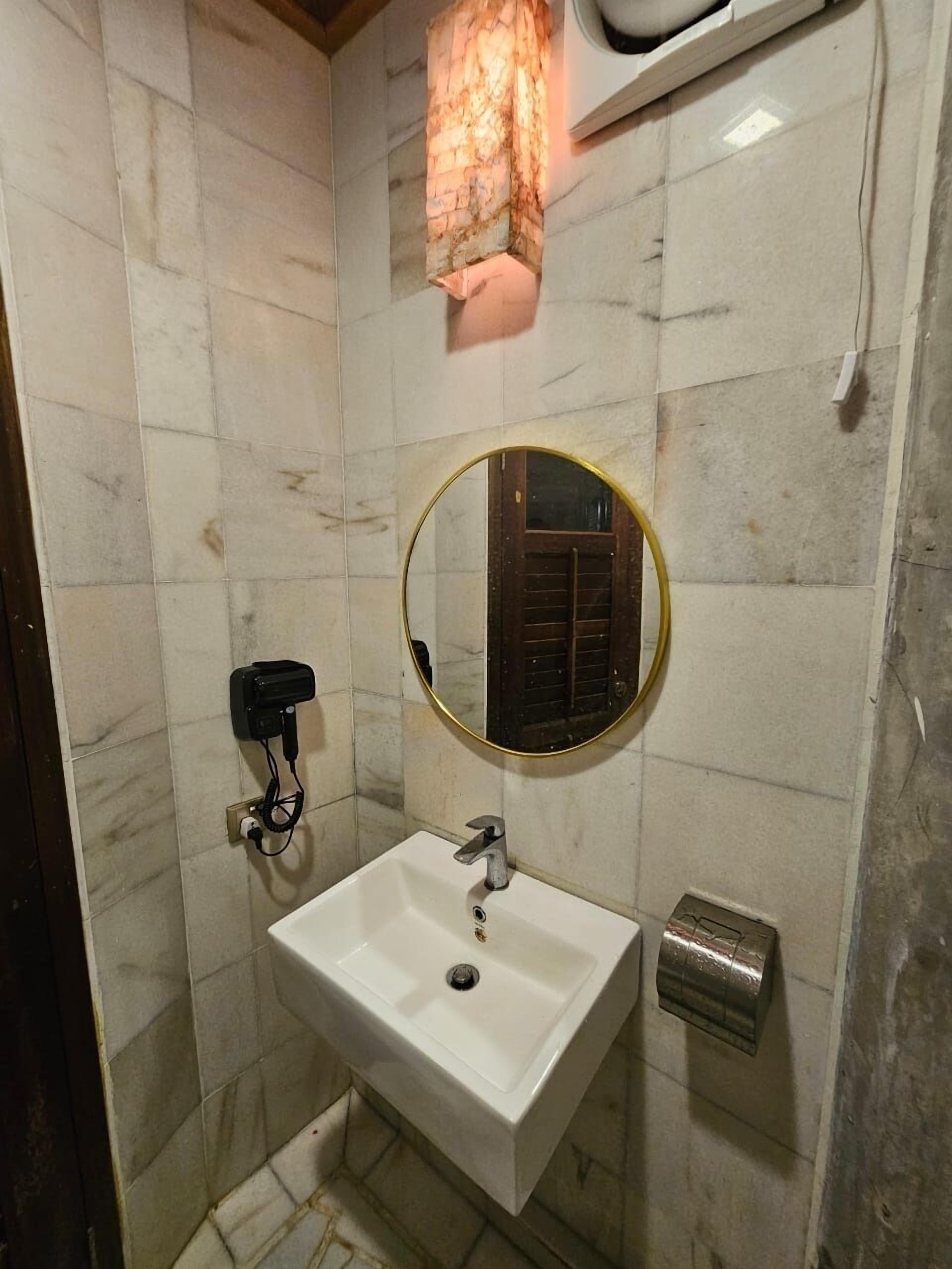 A bathroom with a white sink, a round mirror, a towel rack, and a wall-mounted heater.