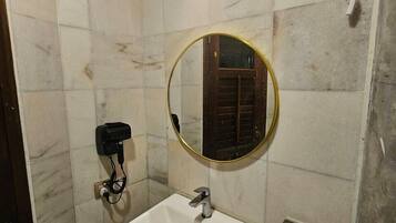 A bathroom with a white sink, a round mirror, a towel rack, and a wall-mounted heater.