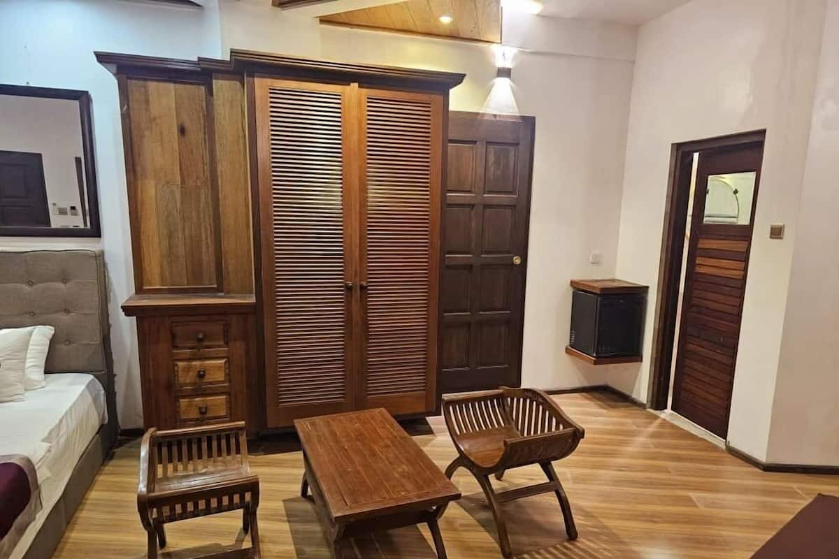 A room with a bed, wooden wardrobe, two wooden chairs, a wooden table, and a television.