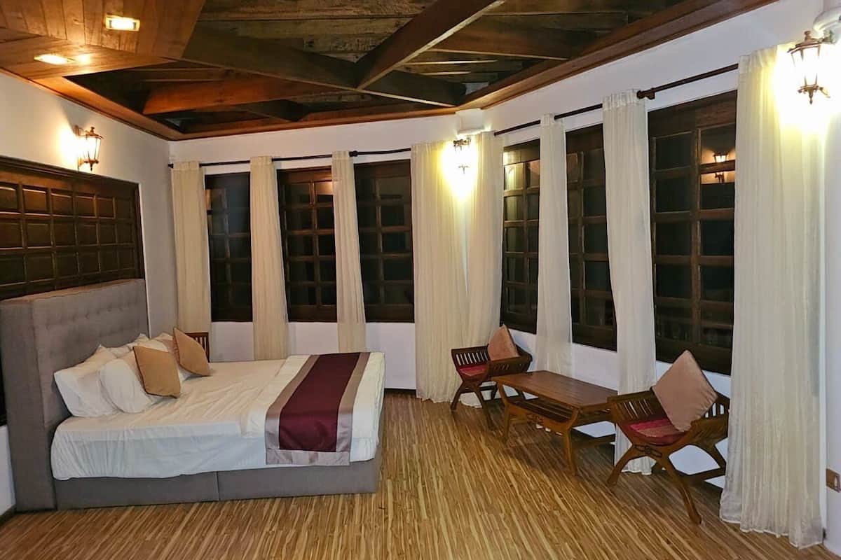 A bedroom with a large bed, wooden floor, and a dining area with chairs and a table.