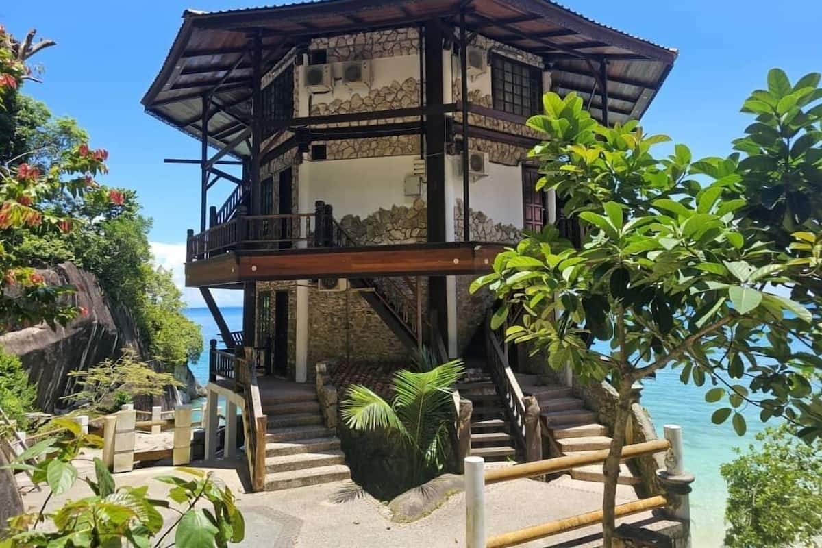 A two-story building with a stone facade, wooden balcony, and a staircase leading to the upper level.