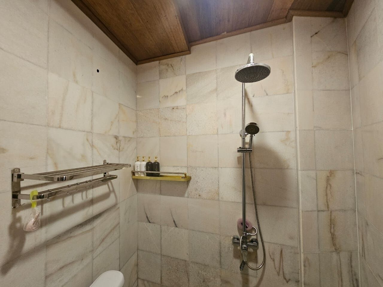 A bathroom with a shower, a towel rack, and a shelf with toiletries.