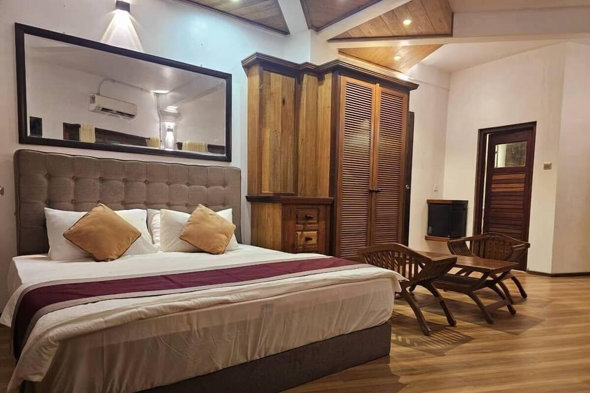 A bedroom with a large bed, a wardrobe, a television, and a dining area.