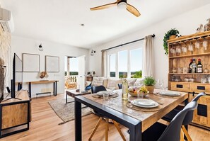 Ein moderner Essbereich mit einem Holztisch, gedeckt für vier Personen, einem Deckenventilator und Blick ins Freie.