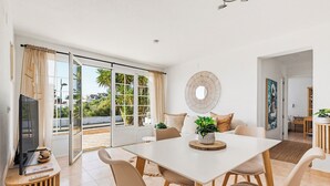 Een moderne woonkamer met een eethoek, grote schuiframen, een flatscreen televisie en een ronde decoratie aan de muur.