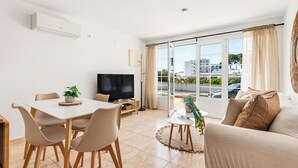 Een moderne woonkamer met een eethoek, een flatscreen televisie en grote ramen voorzien van gordijnen.