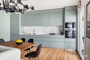 A modern kitchen with light green cabinets, a marble backsplash, and a built-in oven.