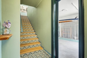 Un escalier orné de carreaux décoratifs et de marches en bois, menant à un balcon doté d’une balustrade.