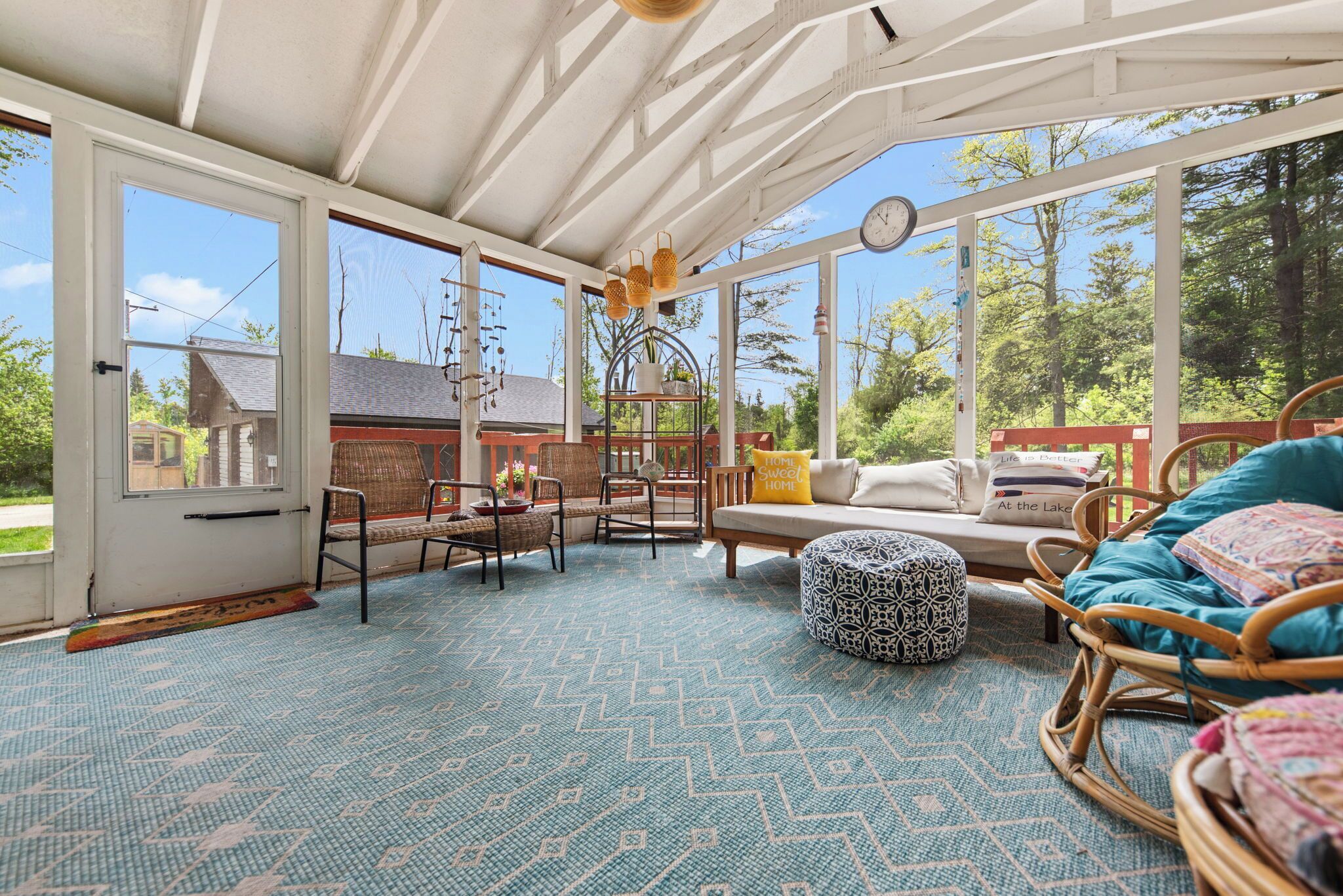 A sunlit room with large windows, wicker furniture, and a patterned carpet.