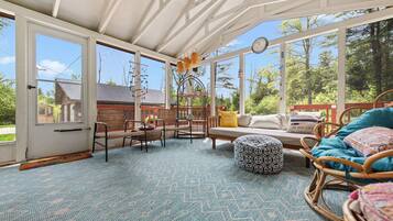 A sunlit room with large windows, wicker furniture, and a patterned carpet.