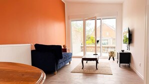 A living room with a sofa, a wooden table, a TV, and a sliding glass door leading to a balcony.