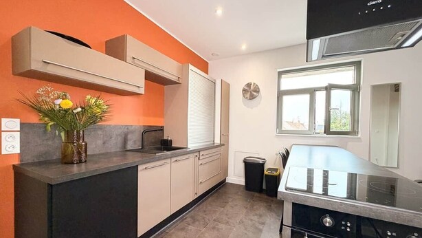 Eine moderne Küche mit schwarzem Arbeitsplatz, beigen Schränken, einem eingebauten Backofen und einem Fenster, das für natürliches Licht sorgt.