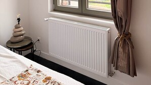 Ein Zimmer mit Fenster, Heizkörper und einem Bett mit gemustertem Überwurf.