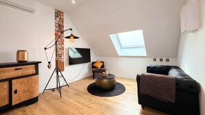 Um apartamento moderno estilo loft com teto inclinado, claraboia, televisão de tela plana, sofá de couro preto, mesa de centro de madeira e luminária vintage.