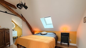Quarto com teto inclinado, claraboia, cama com colcha amarela, mesa de cabeceira pequena com abajur e guarda-roupa de madeira.