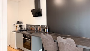 Uma cozinha moderna com parede escura, forno embutido, pia e dois bancos altos.