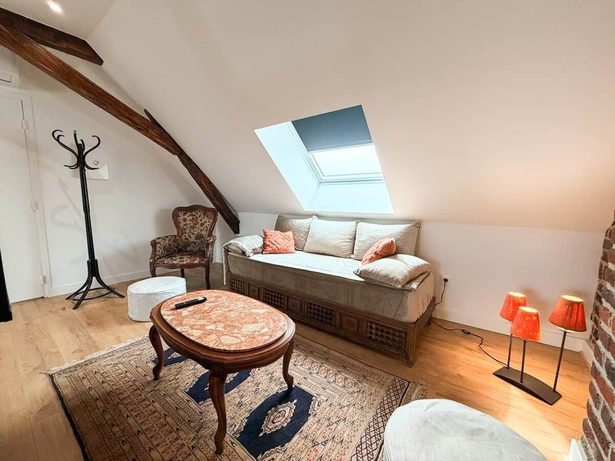 Une chambre à coucher aménagée dans un espace mansardé, avec un plafond en pente, un canapé-lit, une table ronde en bois, un lampadaire et un tapis à motifs.