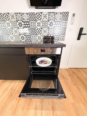 An oven with a digital clock, a tiled backsplash, and a wooden floor. - Le puits du midi - 2-bedroom apartment (Sin-le-Noble)