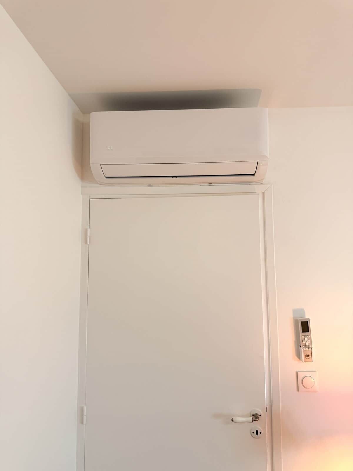 A white door with a wall-mounted air conditioner above it and a doorbell with a push button below.