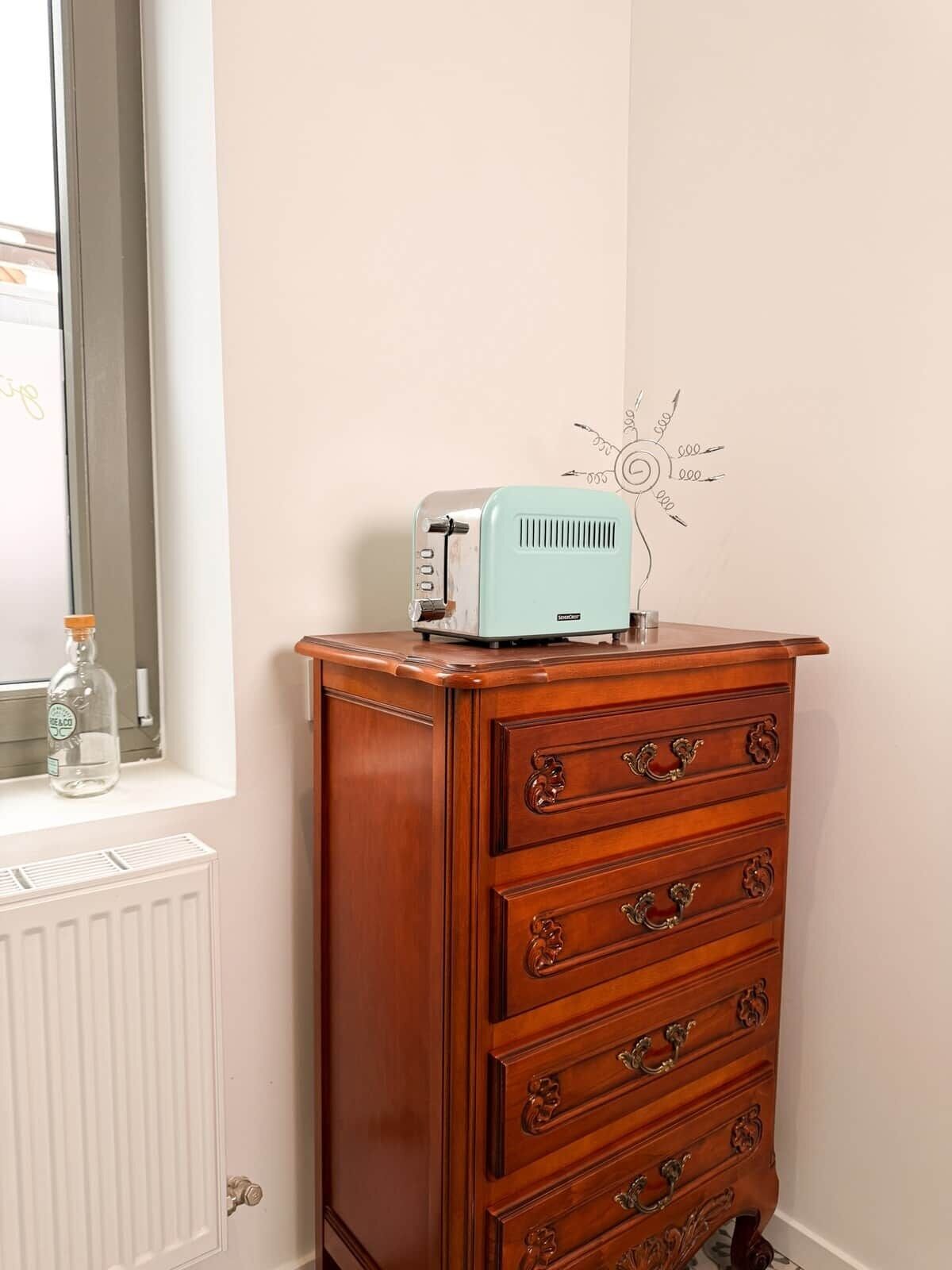 En trækommode med en vintage toaster ovenpå, en vandflaske og en væg med en enkel tegning.