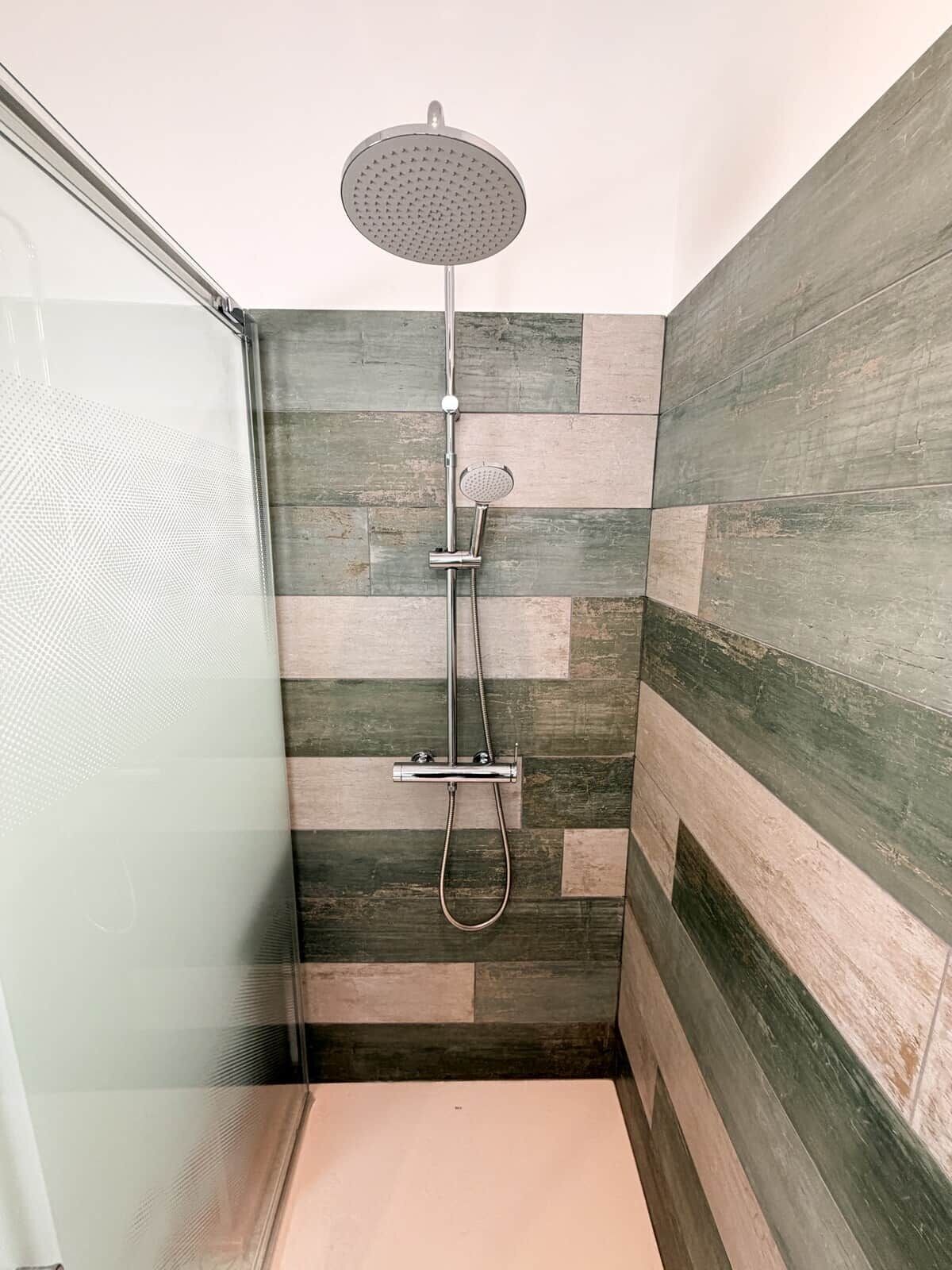 Een douche met een handdouche en een inbouwd regenstortdouche, tegen een wand betegeld met een hongaars bindingspatroon.