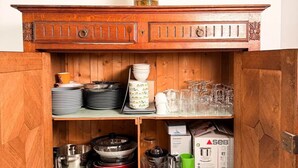 Un mobile in legno con un vaso di fiori sopra, ripiani con piatti, bicchieri e stoviglie da cucina.