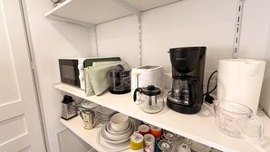 A kitchen with white shelves, a coffee maker, a kettle, a microwave, and various kitchen utensils.