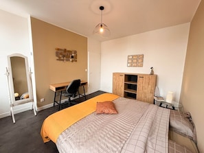 Ein Schlafzimmer mit Bett, Schreibtisch, Stuhl, Kleiderschrank und Spiegel.