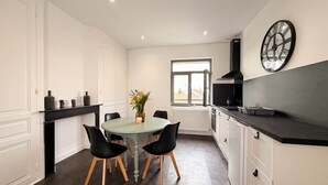 A modern kitchen with a round dining table, black chairs, a clock on the wall, and a window providing natural light.