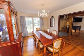Une salle à manger avec une grande table en bois, des chaises, un lustre et un téléviseur en arrière-plan.