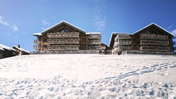A multi-story wooden building with balconies, set against a snowy landscape.