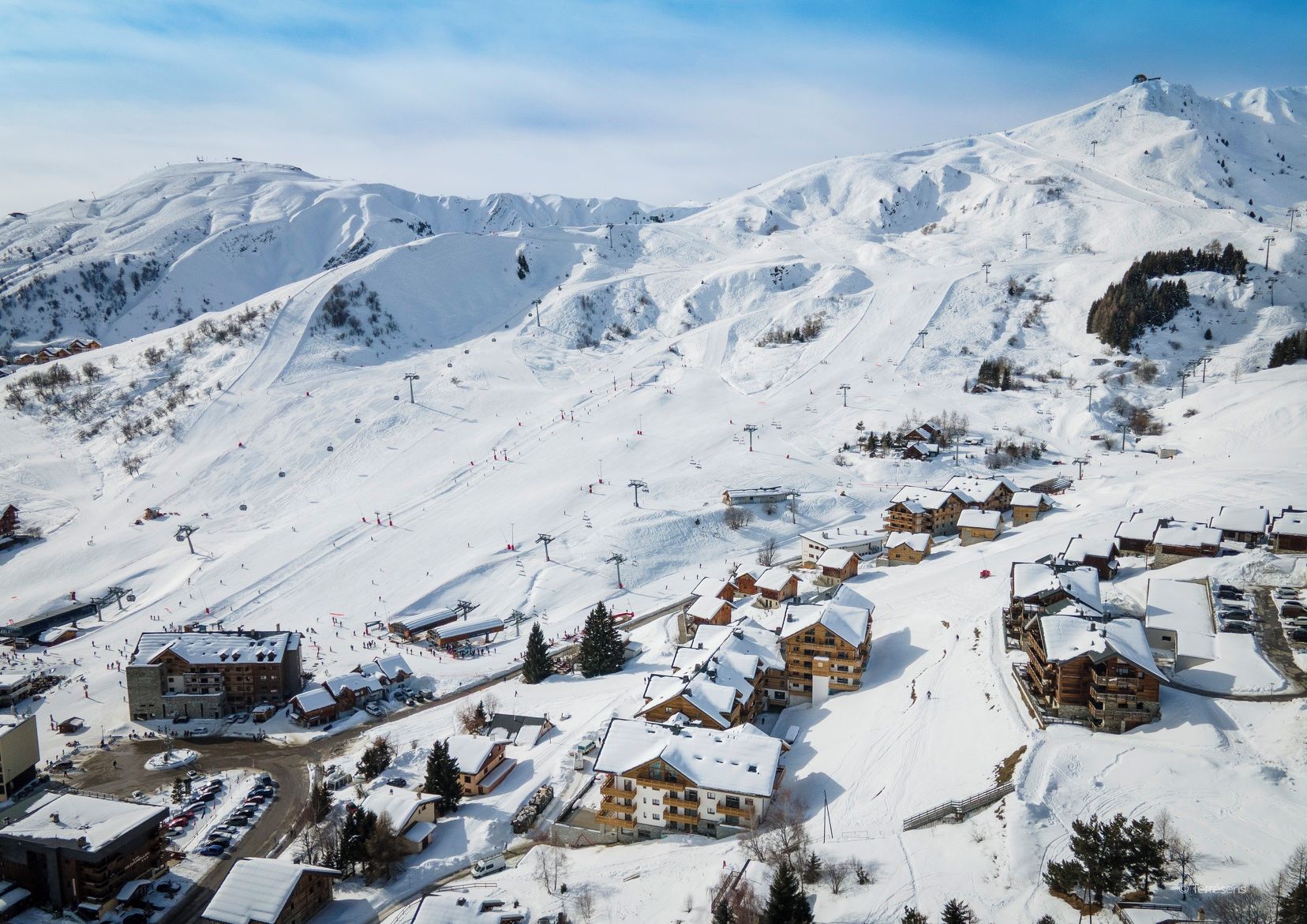 Un pueblo cubierto de nieve en la montaña con pistas de esquí, edificios de madera y un cielo despejado.