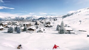 A snowy mountain village with buildings, a ski slope, and a clear sky.
