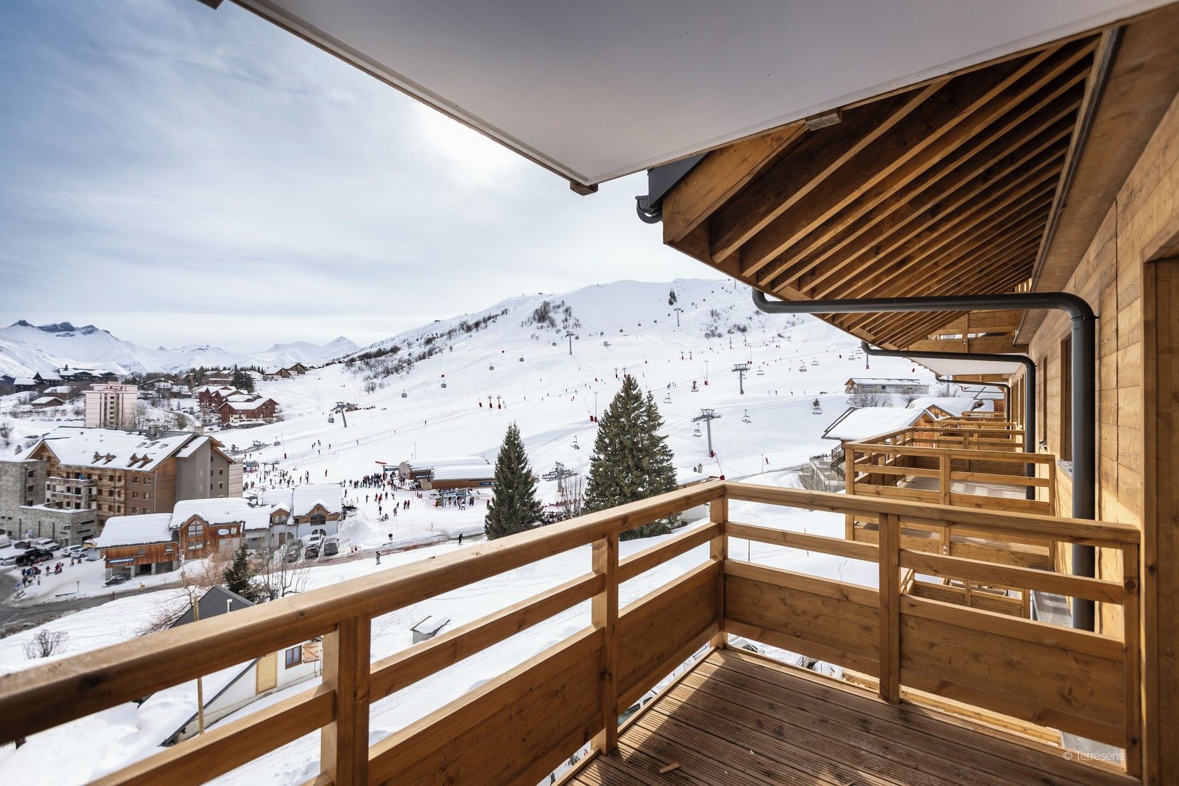 Ein Holzbalkon mit Blick auf eine verschneite Bergstadt und Skipisten.
