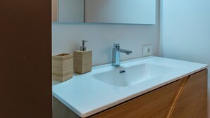 Un baño con lavamanos blanco, tocador de madera y espejo.