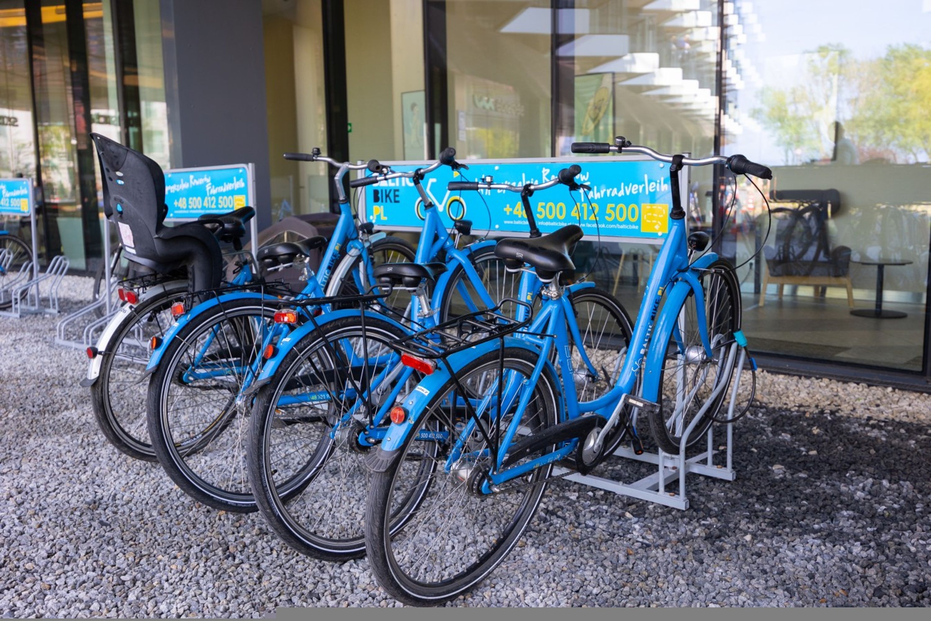 A row of blue bicycles parked in front of a building with a glass facade.