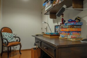 A room with a wooden desk, a chair, and a lamp. There are several board games stacked on the desk. - Quinta da Ponte - Family Refuge in Nature (Viseu)