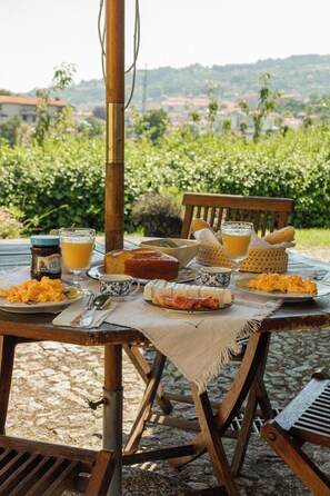 Un tavolo da pranzo all'aperto con diversi cibi e bevande, sullo sfondo di vegetazione e colline.