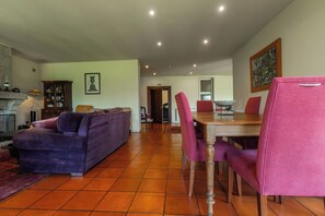 A spacious living room with a purple sofa, a dining table with chairs, and a kitchen area in the background. - Quinta da Ponte - Family Refuge in Nature (Viseu)