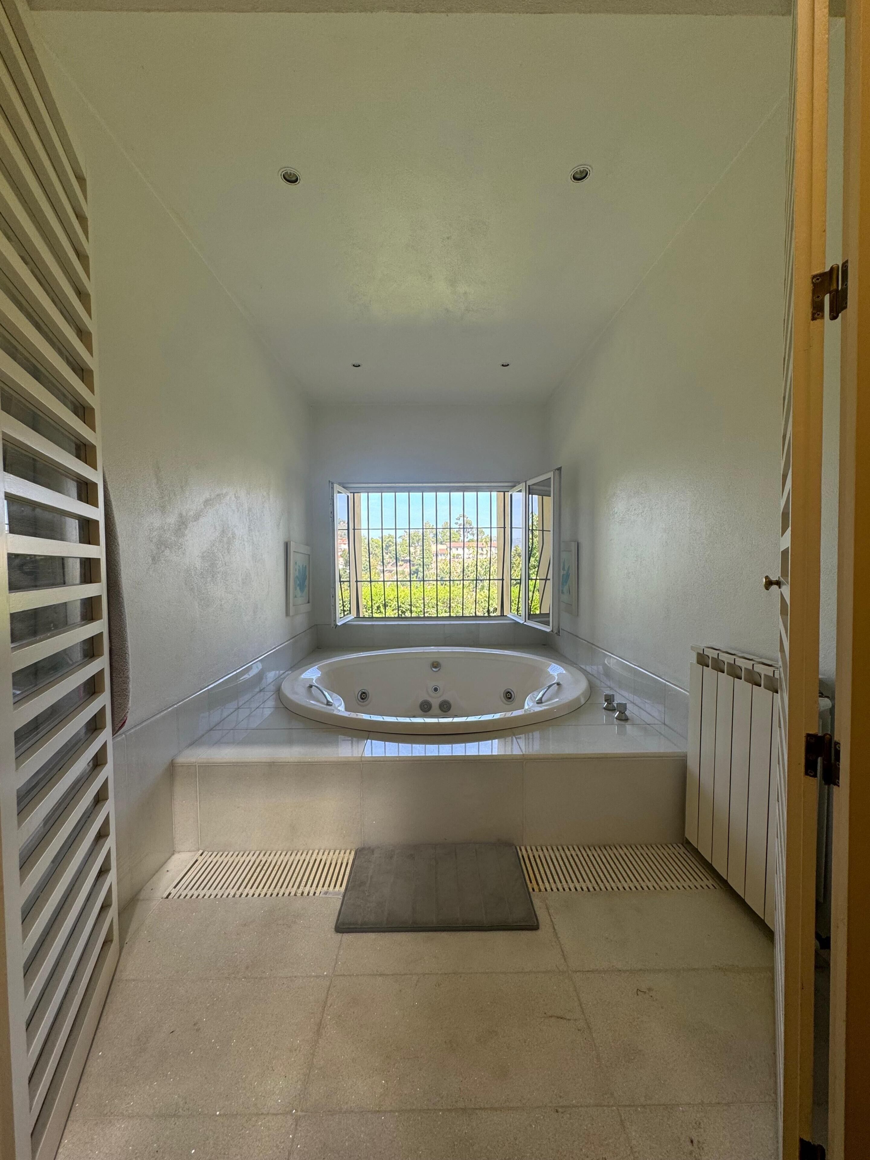 Un baño con una bañera grande, una ventana con vistas, un radiador y un perchero para toallas.