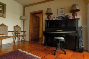 Una stanza con un pianoforte, due sedie, uno sgabello, un tappeto e una porta.