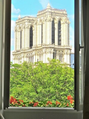 A view of a grand building with multiple columns and arches, viewed through a window with greenery and red flowers in the foreground. - A Duplex In The Sky - Paris — AC (Paris)