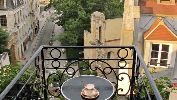 Ein Balkon mit Tisch und Stuhl, der auf eine Straße mit Gebäuden und einem Dom blickt.