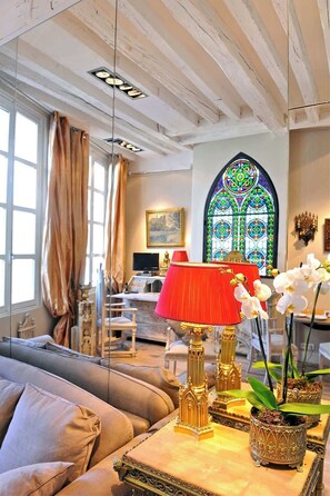 A living room with a sofa, a red lamp, decorative plants, and a stained glass window. - Charming Two Bedroom Suite - AC - At Notre-Dame (Paris)