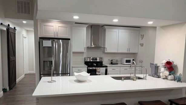 A modern kitchen with white cabinetry, stainless steel appliances, and a central island with stools. - Spacious 4-bedroom farmhouse in tranquil New Port Richey with AC (New Port Richey)