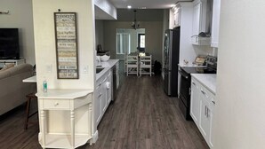 A modern kitchen with white cabinetry, a central island, and a dining area with a white table and chairs. - Spacious 4-bedroom farmhouse in tranquil New Port Richey with AC (New Port Richey)