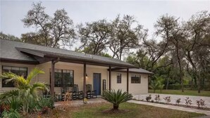 A single-story house with a porch, a door, and a small garden area with plants and a palm tree. - Spacious 4-bedroom farmhouse in tranquil New Port Richey with AC (New Port Richey)
