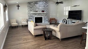 A living room with a fireplace, sofas, a television, and a ceiling fan. - Spacious 4-bedroom farmhouse in tranquil New Port Richey with AC (New Port Richey)