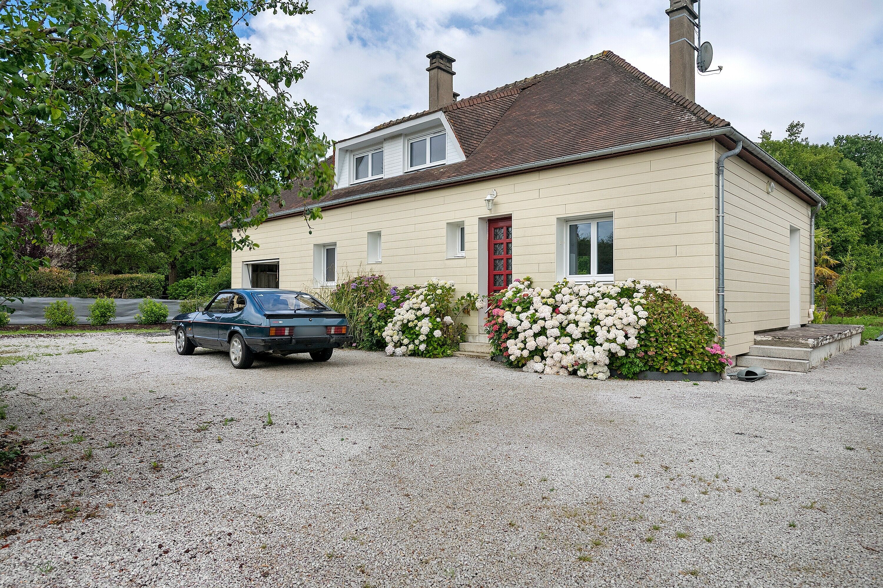 A single-story house with a red door, a gravel driveway, and a parked car.