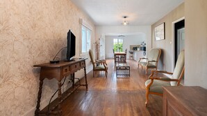 Una habitación amplia con piso de madera, una mesa de comedor con sillas, un televisor sobre un mueble de madera y un ventanal grande.